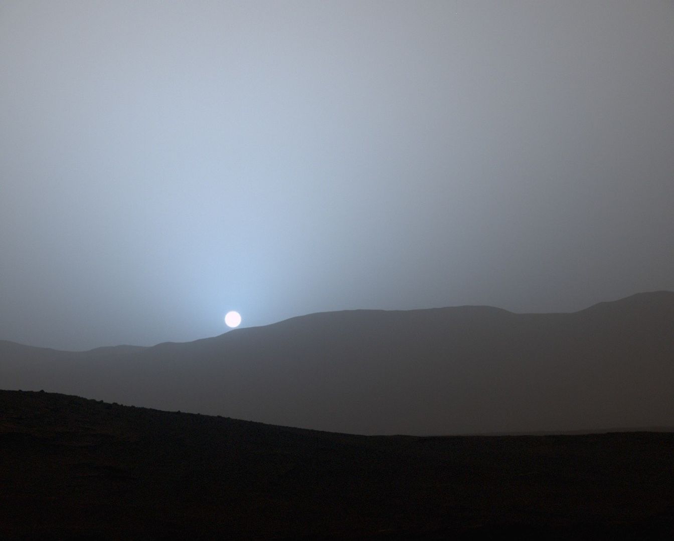 Atardecer fotografiado por Curiosity en el cráter Gale: un halo azulado rodea al Sol sobre el horizonte de Marte.